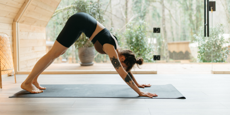 Woman doing "downwards dog" position on a black yoga mat.