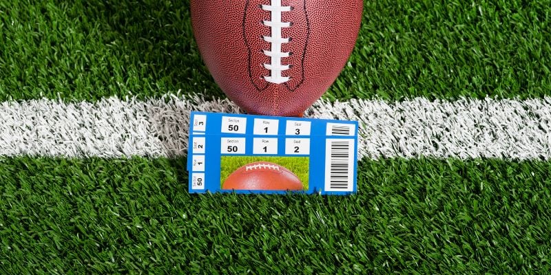 pair of football tickets leaning against a football on AstroTurf 