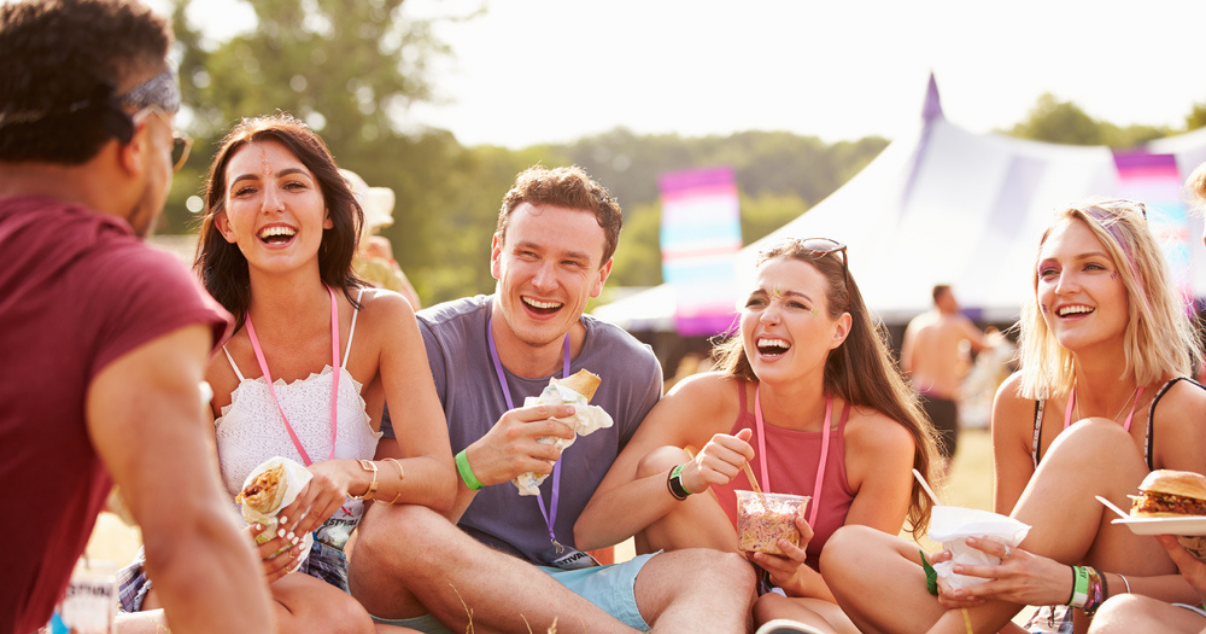Group of friends happily eating food at a music festival while sitting on the grass