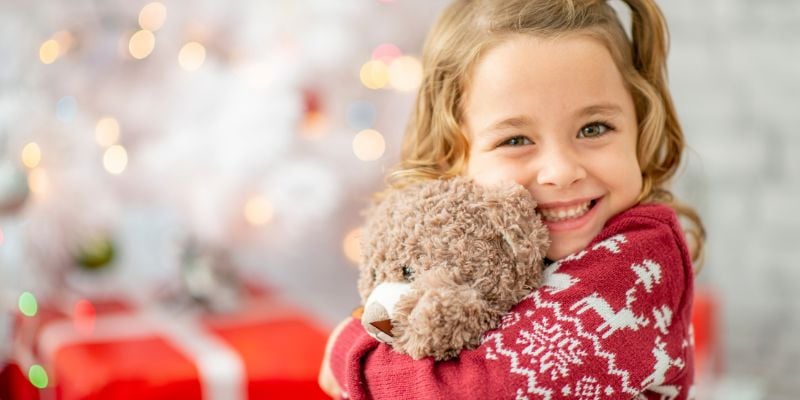 Beautiful child hugging a teddy bear enjoying Christmas morning in front of a Christmas tree