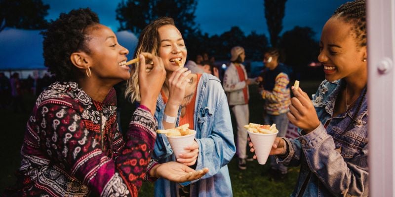 Three happy young women enjoying french fries at a nighttime festival