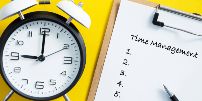 A black and white clock next to a clipboard that says Time management in front of a yellow background. (1)