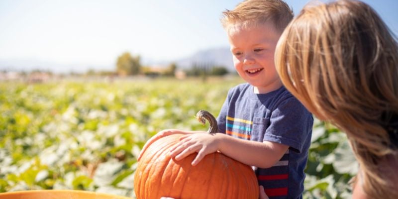 smiling young bot holding a pumpkin on a farm with his mother in the foreground