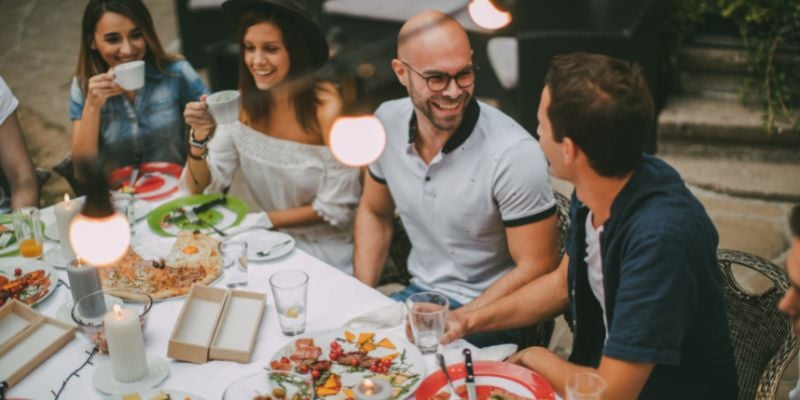 happy smiling people around an outdoor table with cafe lights hanging above