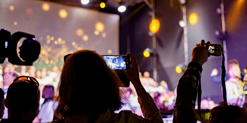 People holding their phones up while recording a concert at an indoor venue. (1)