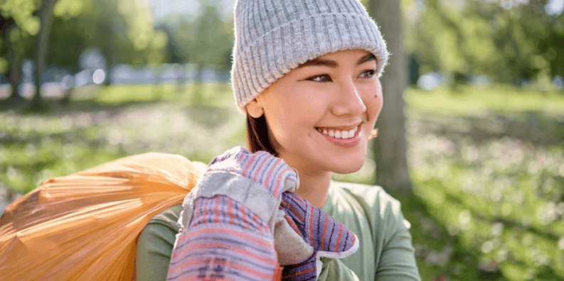 A close-up of a woman smiling and carrying trash bag. 