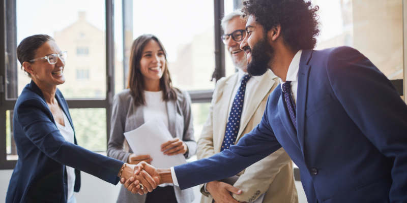 Man giving a woman a handshake, dressed in business professional clothes.