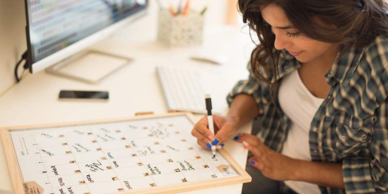 Woman writing on a whiteboard calendar.