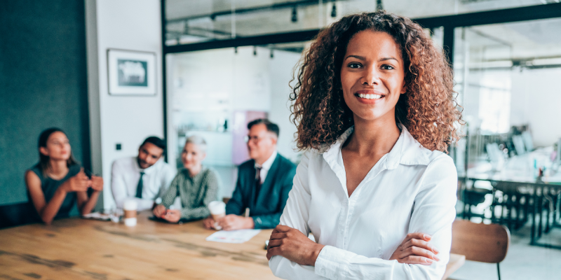 Woman standing confidently in front of a table with 4 people sitting down.