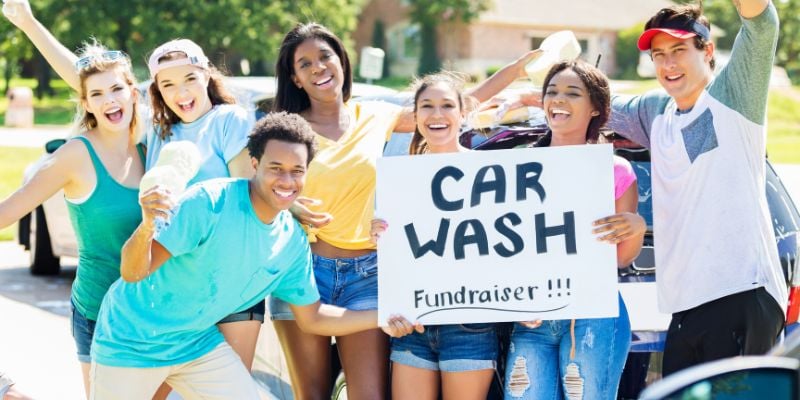 young teens smiling and holding a car wash sign for a fundraiser