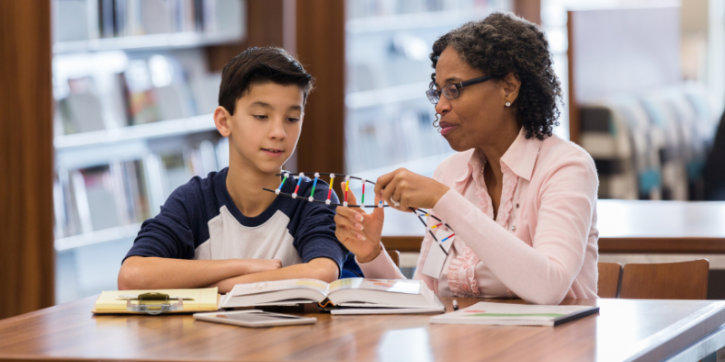 Woman sitting at a desk with a child teaching him science.