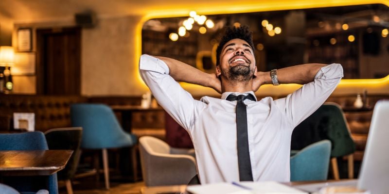 man smiling and looking upwards with hands reached behind his head, in a restaurant