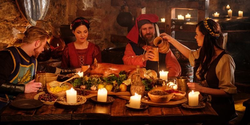 people dressed in renaissance attire enjoying a meal by candlelight