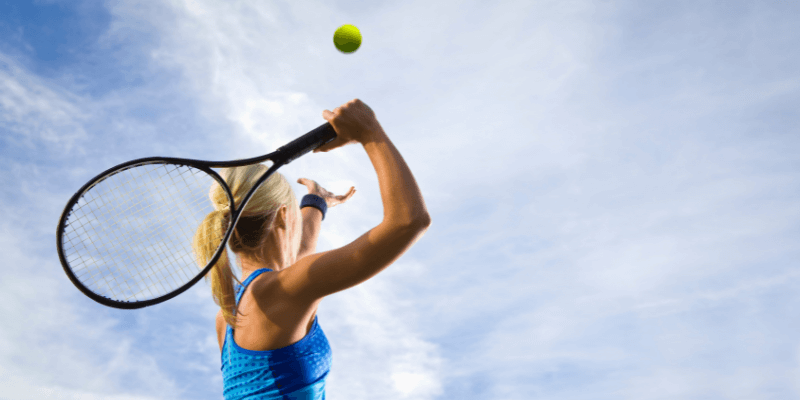 A woman throwing a tennis ball into the air while reaching her arm back with a racket getting ready to hit it.   (1)