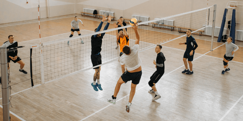 Two teams playing volleyball. They are reaching up to hit the ball.  (1)