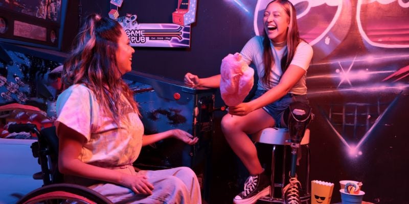 Two young women sitting in an arcade laughing and enjoying cotton candy
