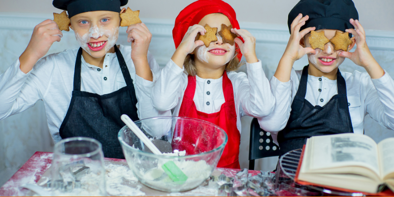 Children baking Christmas cookies wearing cute aprons and posing with cookies on their faces