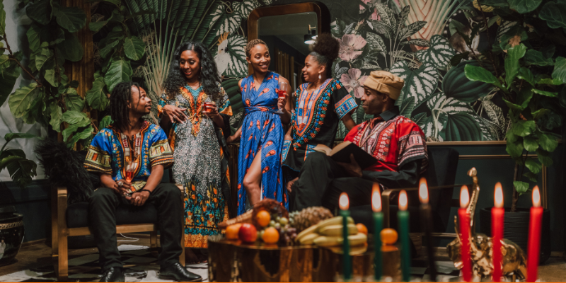 Group of people celebrating Kwanzaa posing against a green aesthetic background with lots of plants