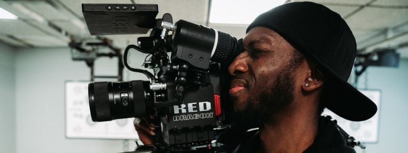 Cameraman in denim jacket looking through the lens of professional film camera