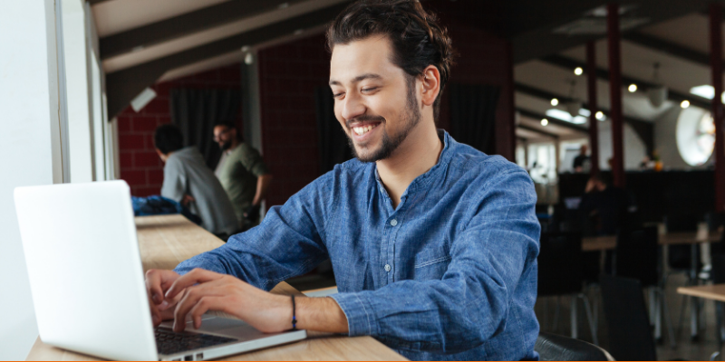 Happy young man wearing denim button-down shirt using laptop computer indoors