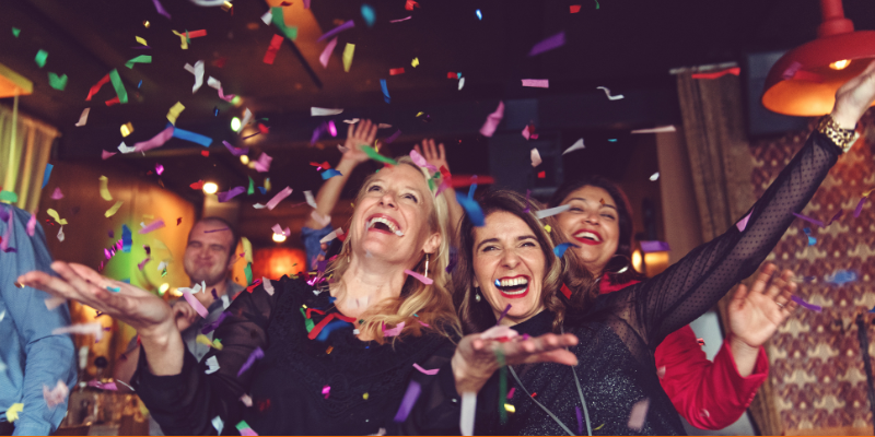 Three women throwing confetti in a bar at a New Years Eve party