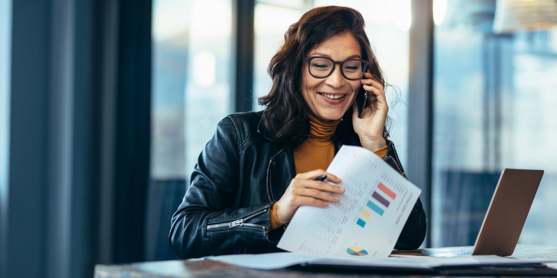 Happy businesswoman talking on the phone while going through some paperwork in an office