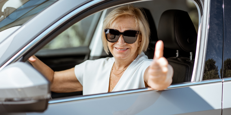Happy senior woman driver giving a thumbs up out the front window of her car