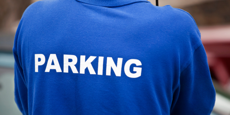 Parking attendance wearing blue polo shirt with parked car in the backgroun