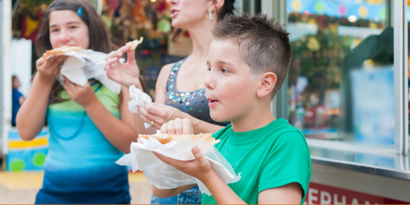 Woman and two kids eating funnel cakes at a fair