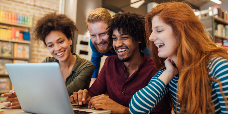 Happy young adults using laptop in a library