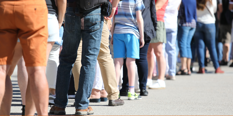 Long queue of people waiting in line outside in warm weather, seen from the shoulders down