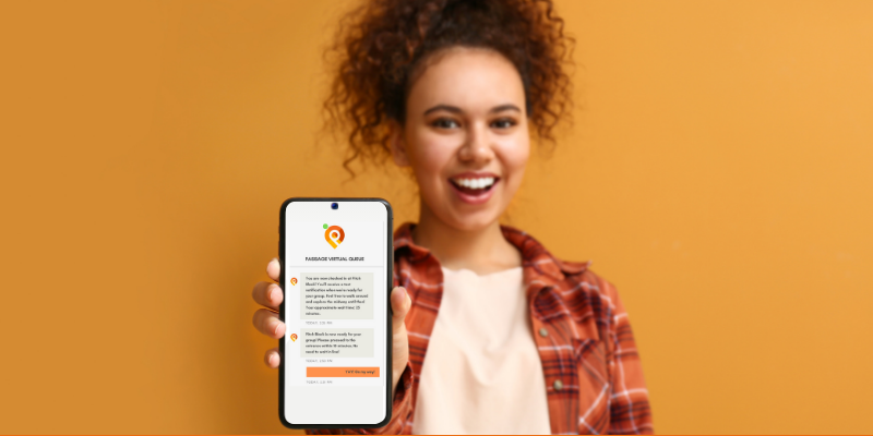 Young African American woman wearing orange flannel shirt holding up a mobile phone with Passage virtual queue message on the screen