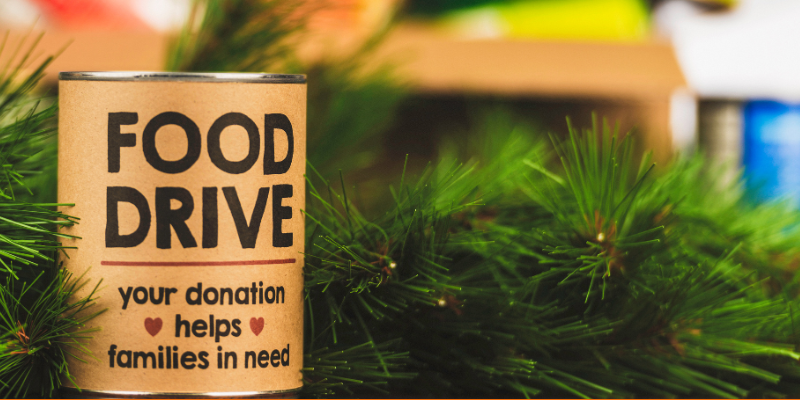 Holiday canned food drive, can with food drive written on the label sitting among evergreen branches