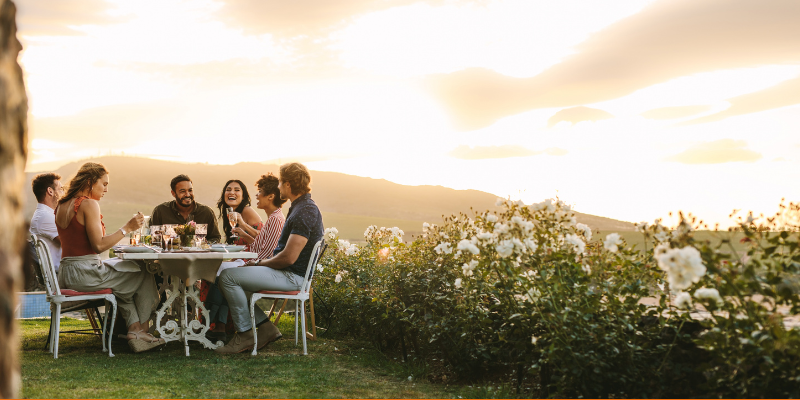 Group of friends hanging out at an outdoor dinner party next to a field of flowers