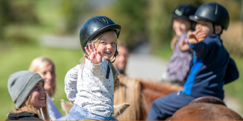 Smiling children waving while taking horseback riding lessons