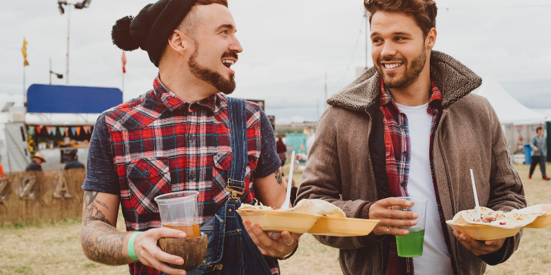 Two men walking together at a festival holding drinks and food