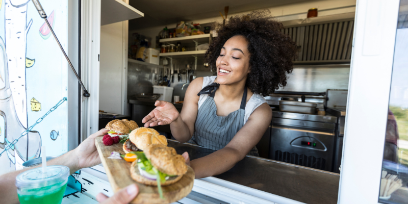 Woman chef handing a customer a plate of three sandwiches from a food truck
