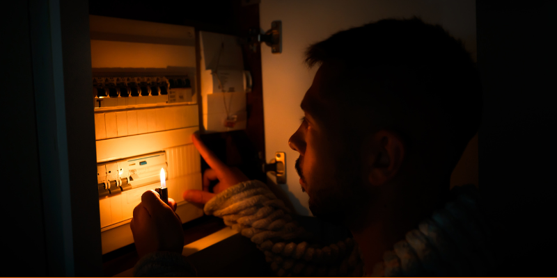 Man with lighter in total darkness investigating a fuse box