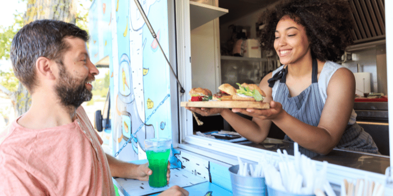 Happy African American Woman Selling Burgers from Food Truck to Customers