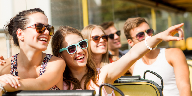 Group of smiling friends traveling by tour bus wearing sunglasses