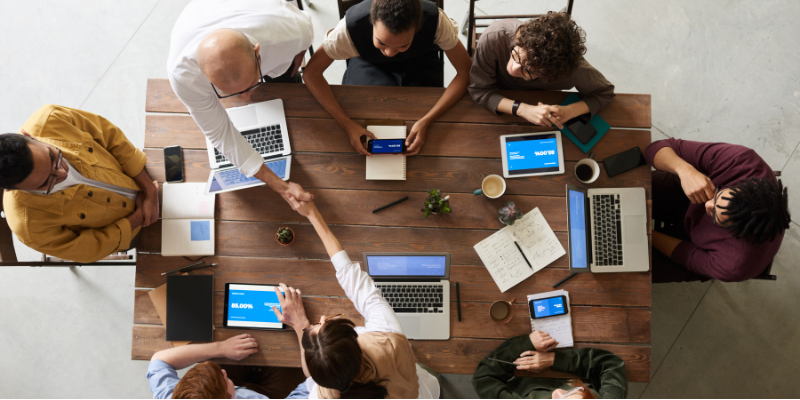 Birds eye view of a diverse team of professionals working on laptops and mobile devices around a table