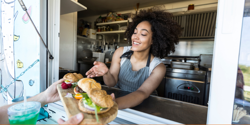 Female chef handing a trio of burgers to an unseen customer from her food truck