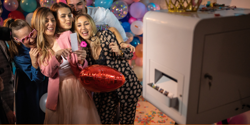 Group of young friends having fun taking photos at a photo booth machine and looking at photos