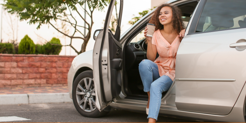 Young African American woman getting out of car with a cup of coffee in hand
