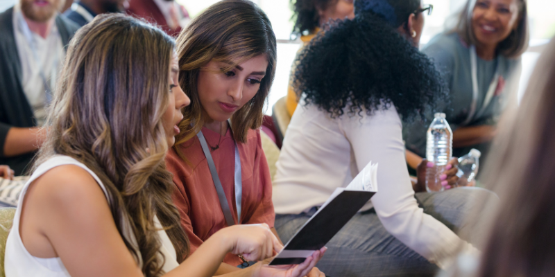 Female business conference attendees reviewing the programs together, seated