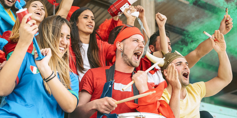 Sports fans cheering while watching a soccer match and using various noise machines