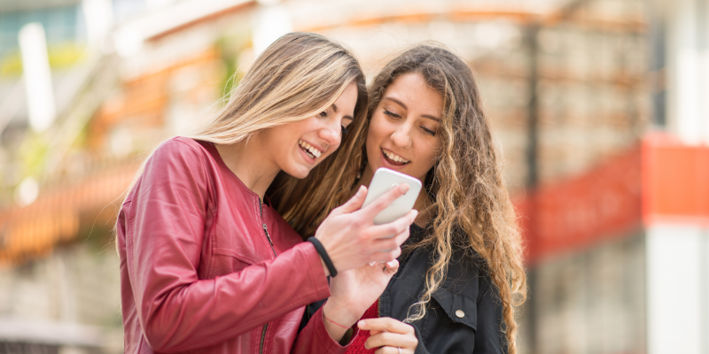 Two smiling young women using a mobile phone in an outdoor city