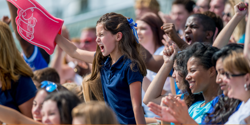 Young girl with a foam finger among a crowd of sports fans cheering during a sports game