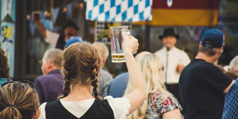 Woman standing in a crowd at Oktoberfest celebration holding up an almost-empty beer stein