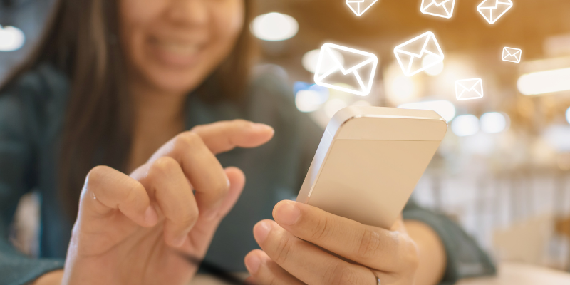 Close-up shot of a womans hands tapping on mobile device while digital neon white envelopes float away